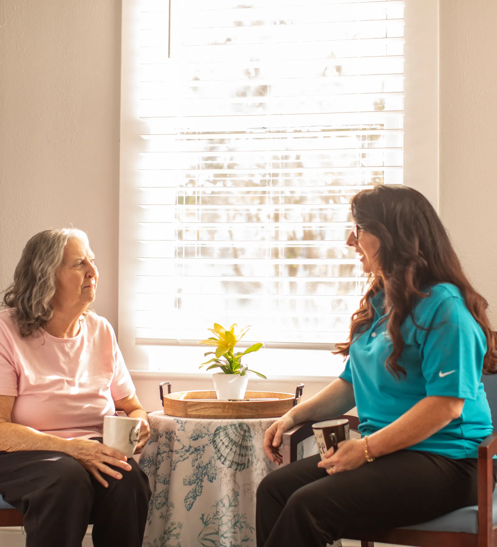 A Sandcastle caregiver chatting with an older woman over coffee