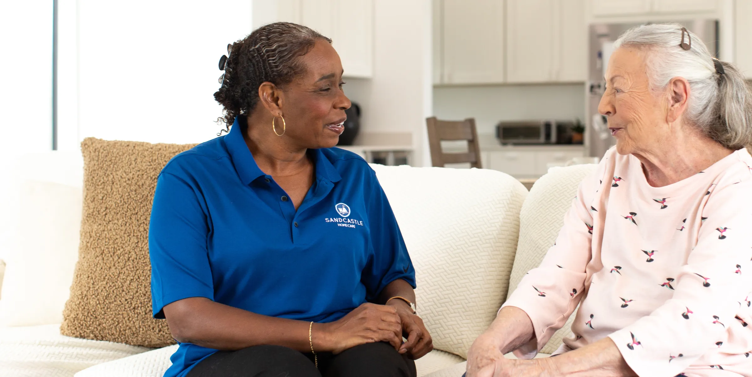 A Sandcastle caregiver chatting with an older woman on her sofa at home