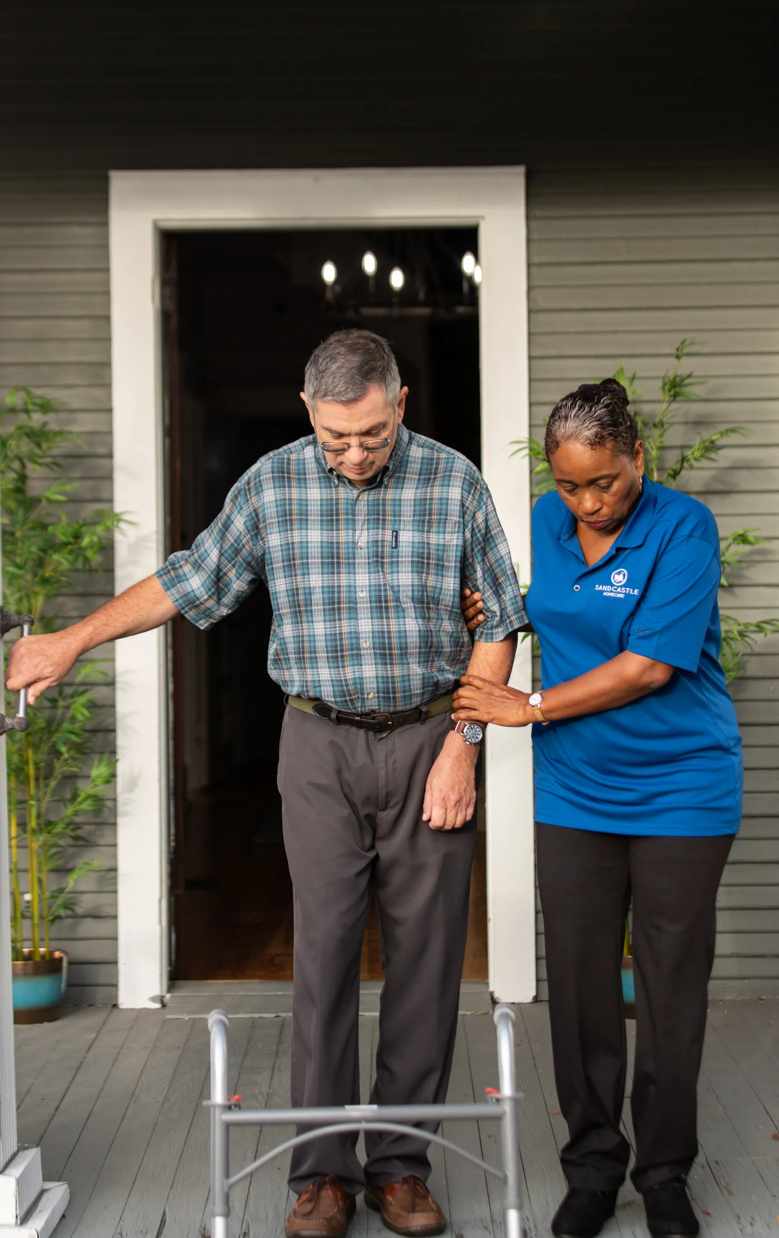 A caregiver helping an older man with a walker down his porch steps