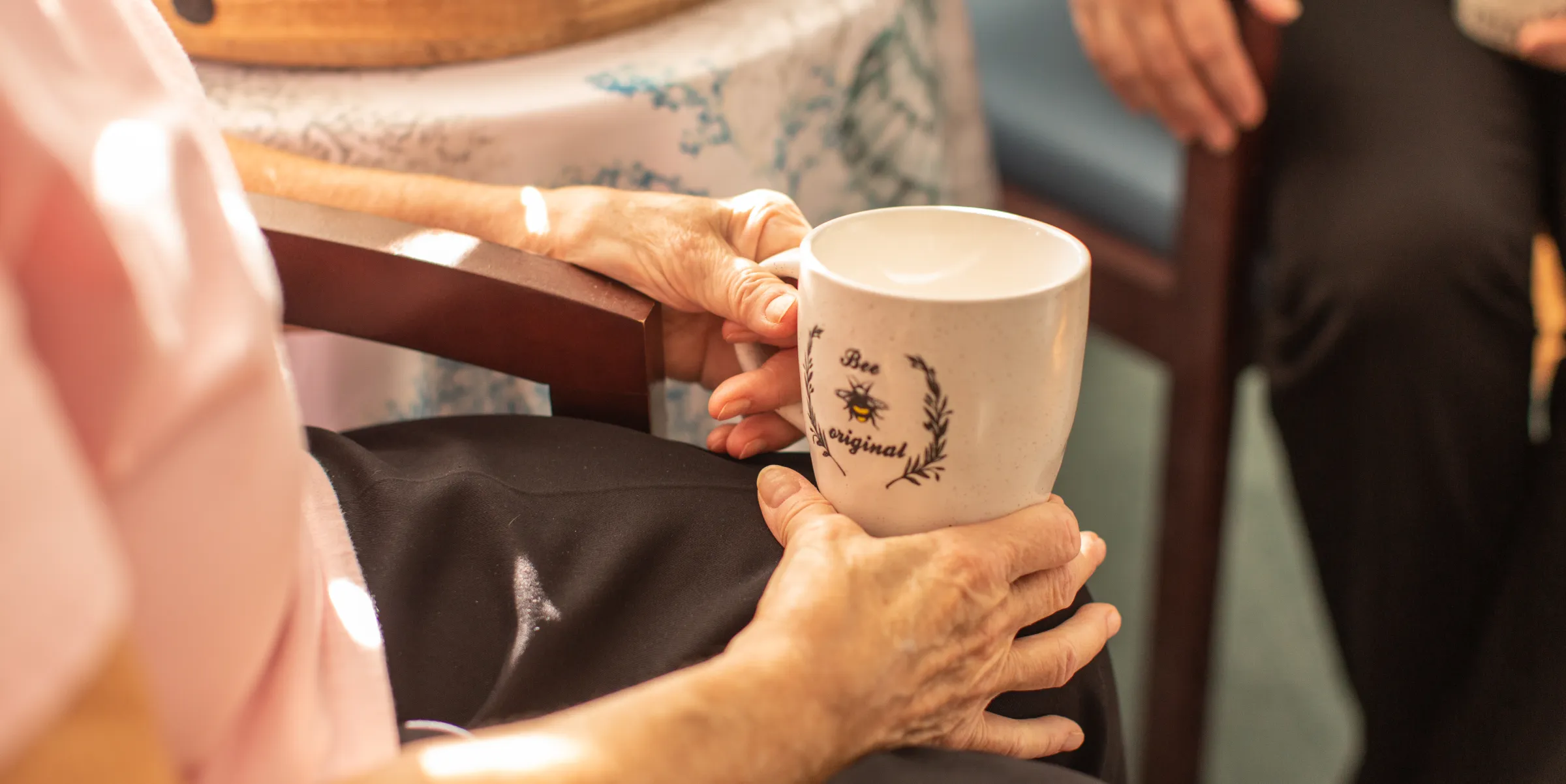 A caregiver's hands passing a coffee mug to an older woman